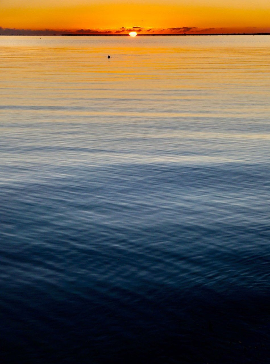 Vibrant orange sunset over calm blue water with gentle ripples and a distant horizon.